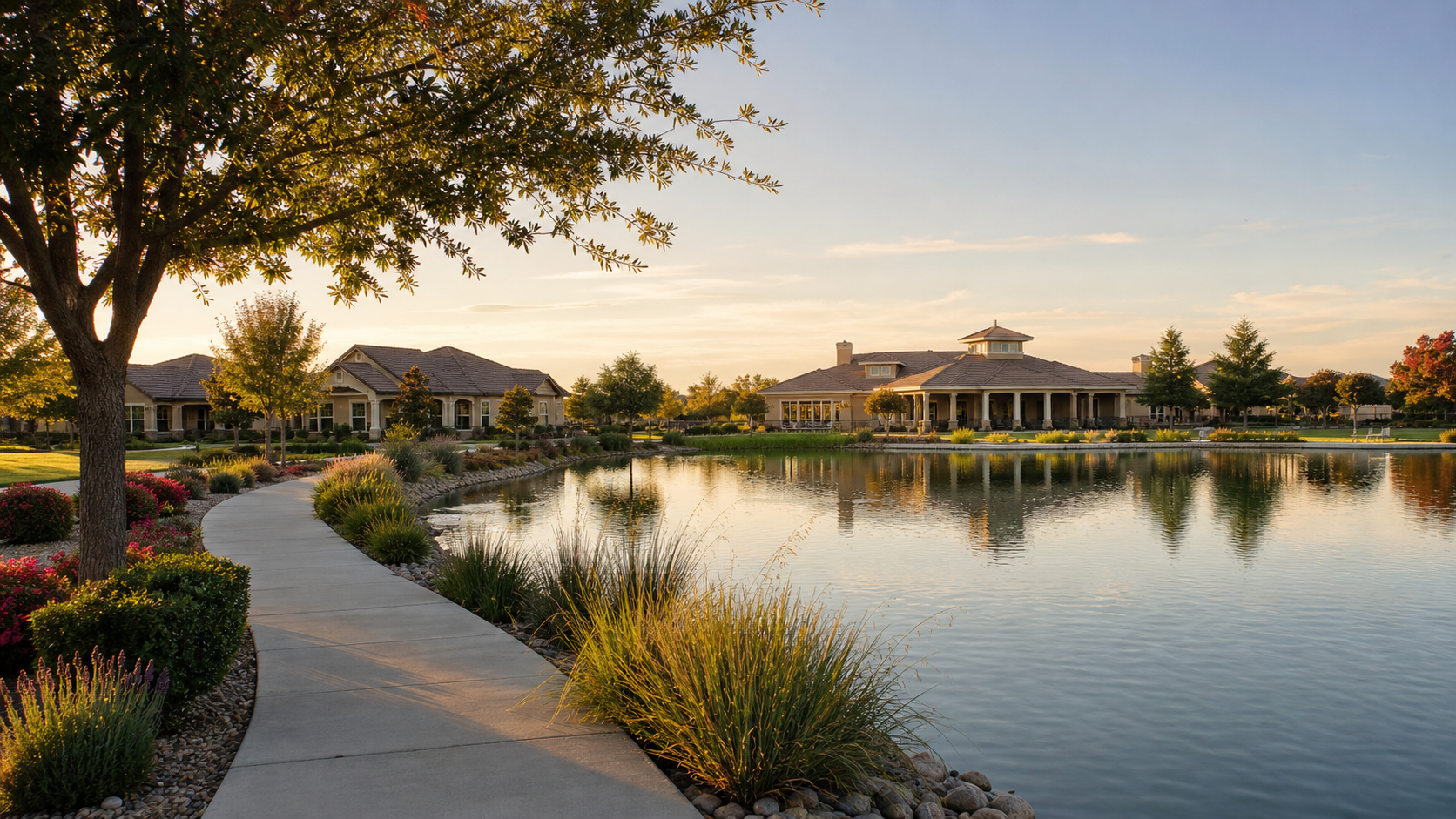 Path along the lake at Del Webb at Woodbridge, with single-story homes and the clubhouse in the evening light